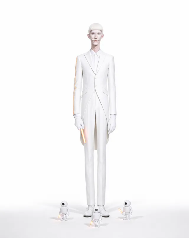 V4GN3R on a pure white seamless in a white tailcoat suit, holding an orange light stick, three small white robots at his feet.